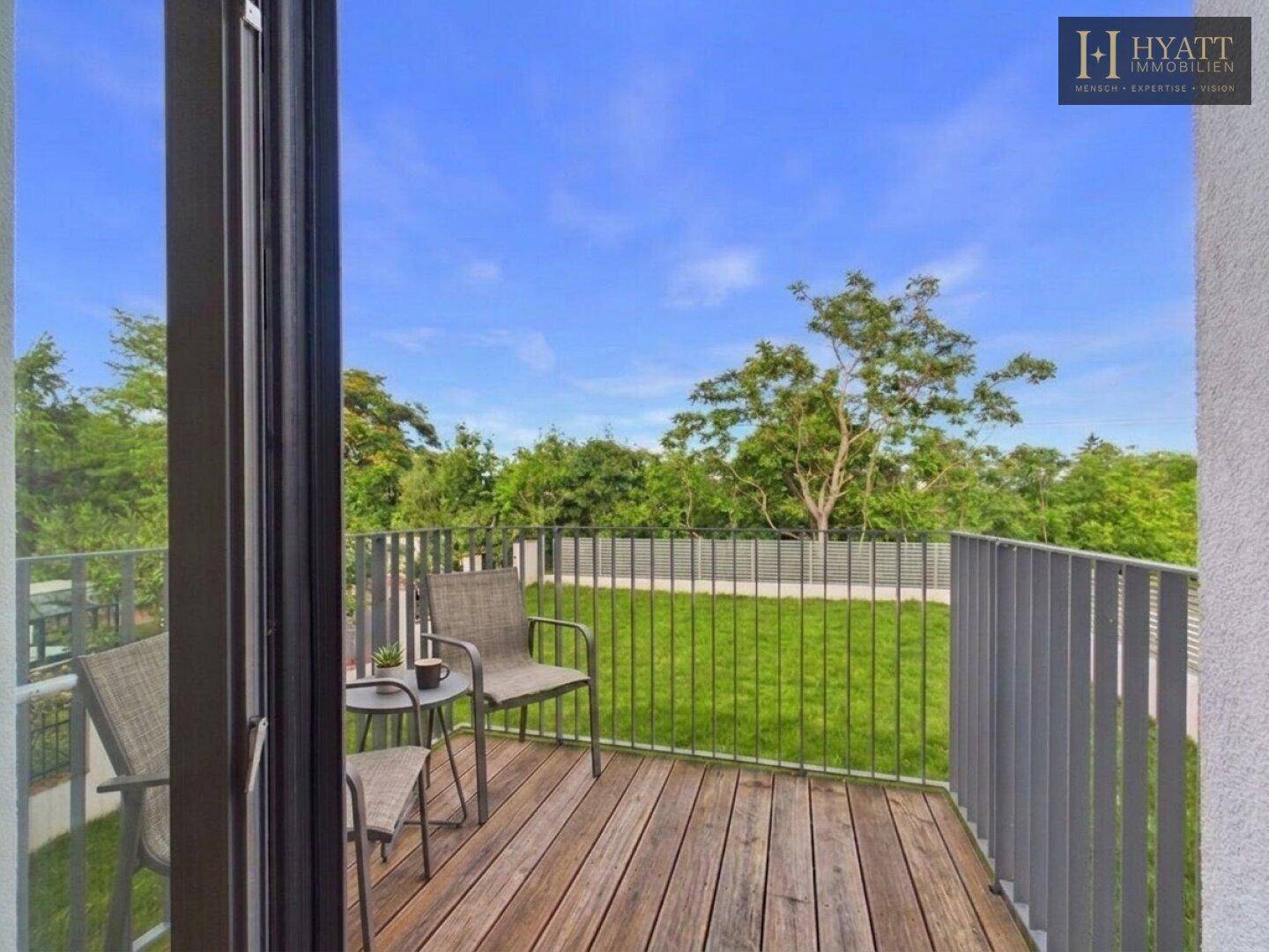 Kleiner Balkon mit Holzboden und Metallgeländer, ausgestattet mit einem Tisch und Stühlen.