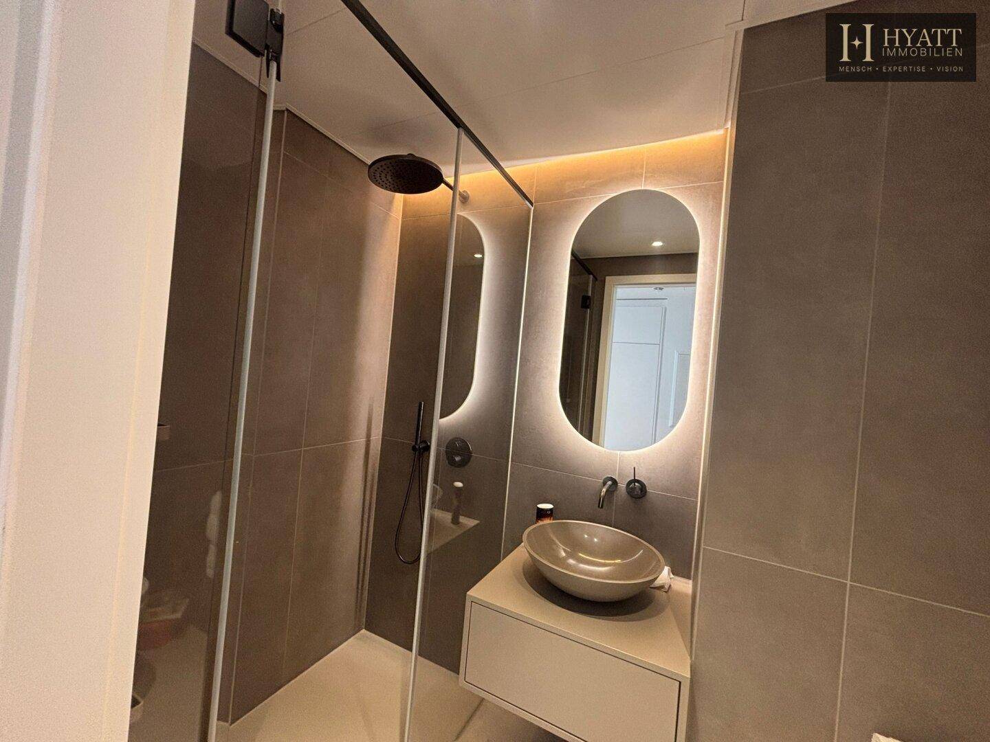 Modernes Badezimmer mit begehbarer Dusche, Aufsatzwaschbecken und beleuchtetem Spiegel.