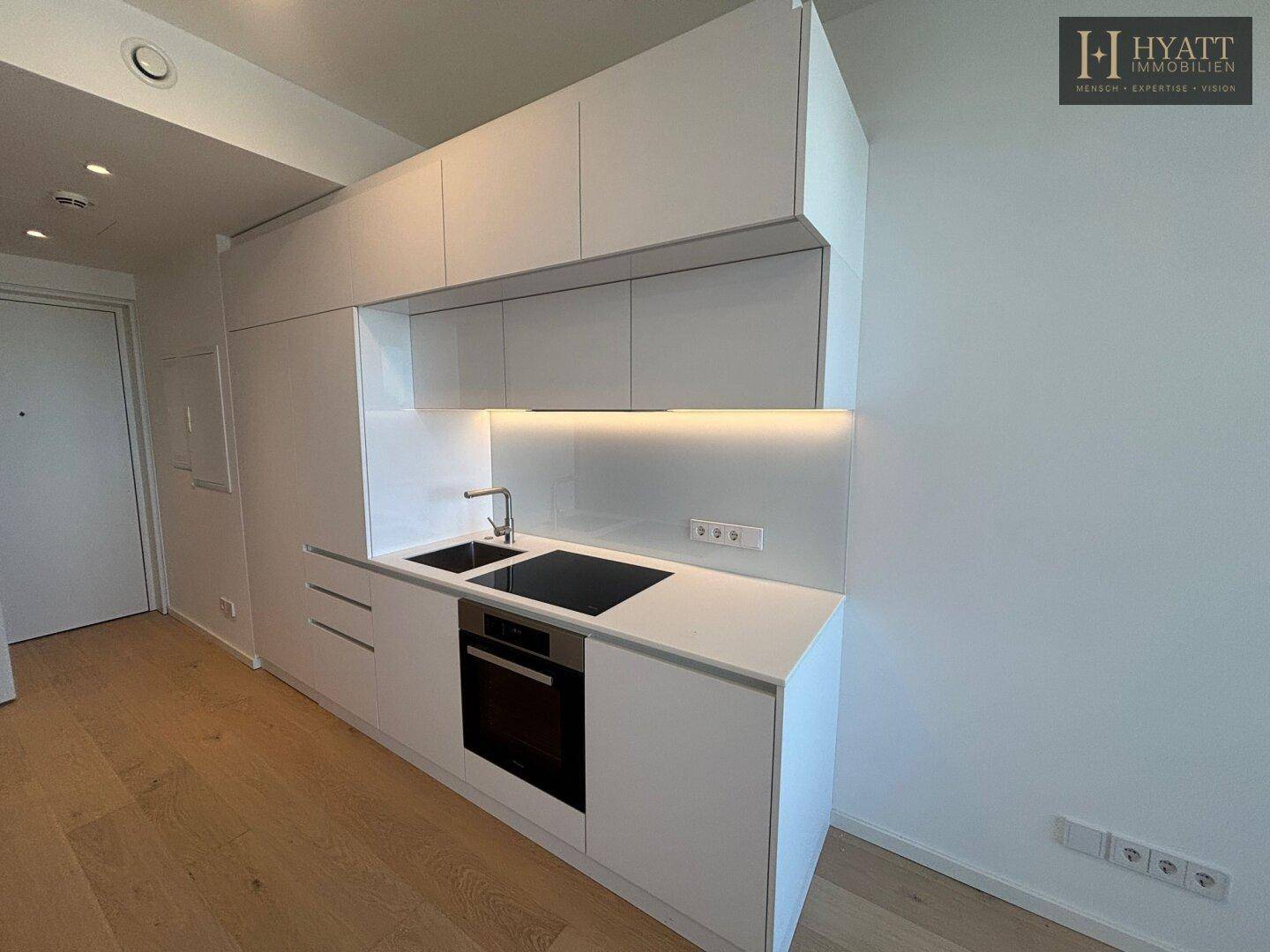 Moderne Küchenzeile mit weißen Hochglanzschränken, Spüle und integriertem Kochfeld und Backofen.