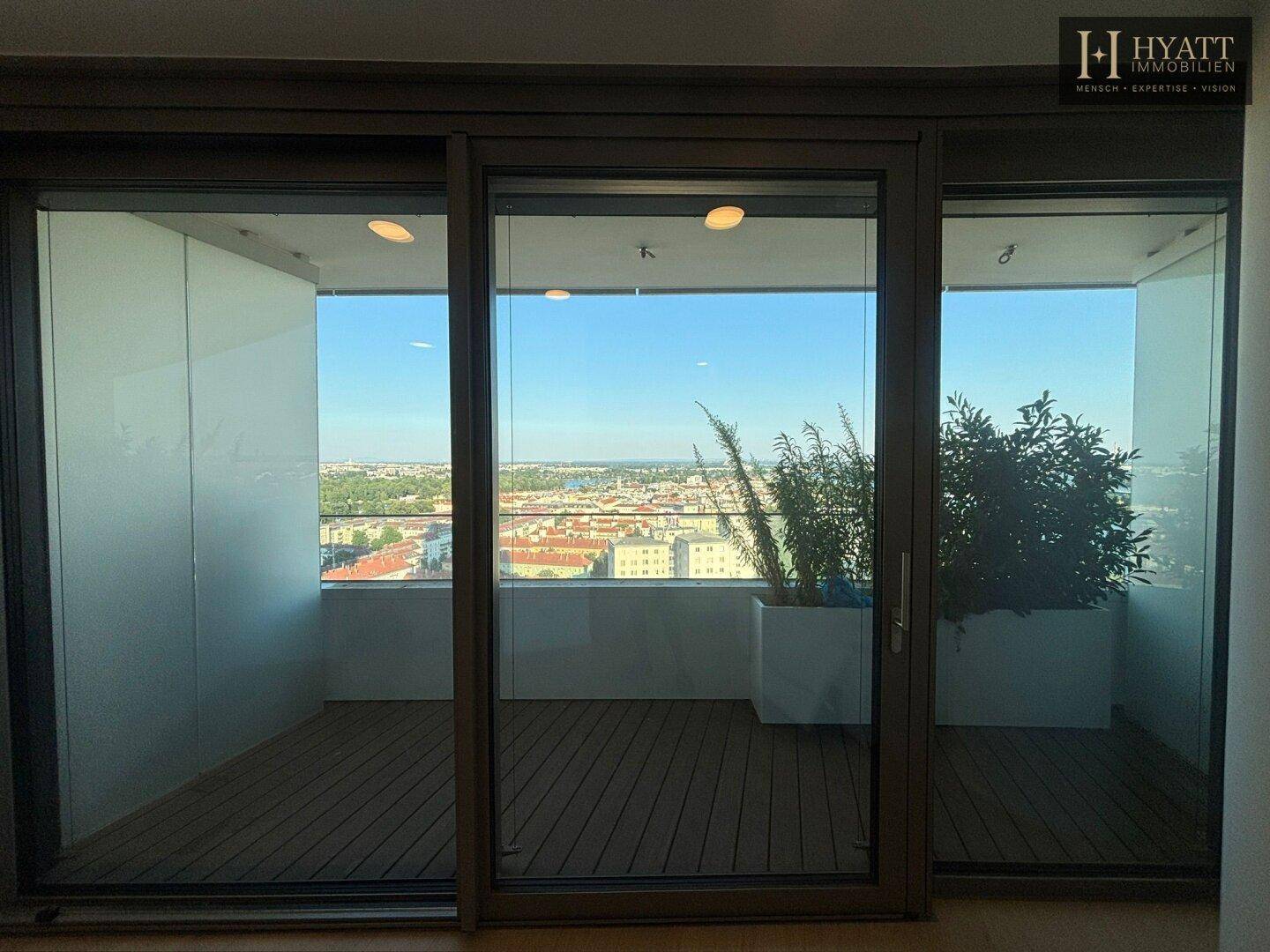Geräumiger Balkon mit Holzdeck und Glasgeländer, bietet einen weiten Stadt- und Flussblick.
