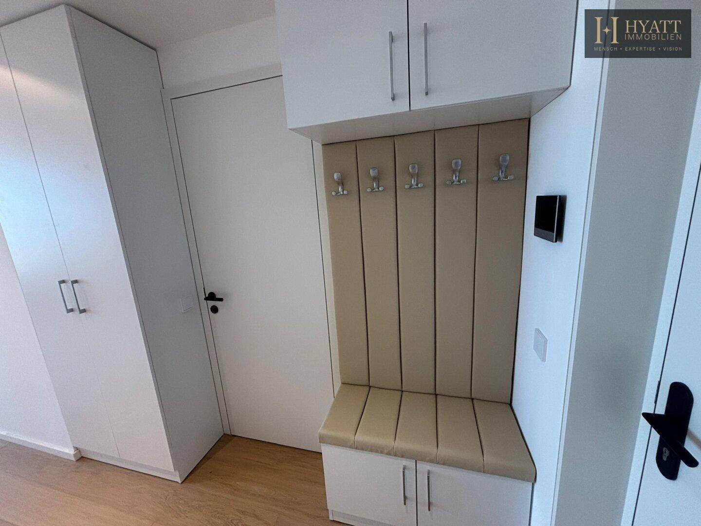 Eingangsbereich mit Einbauschränken und einer gepolsterten Sitzbank mit Garderobenhaken.