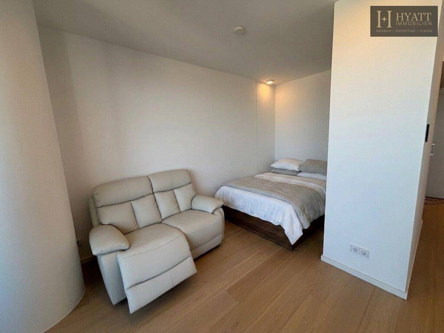 Gemütliches Schlafzimmer mit Einzelbett, kleinem Sofa und hellem Holzboden.