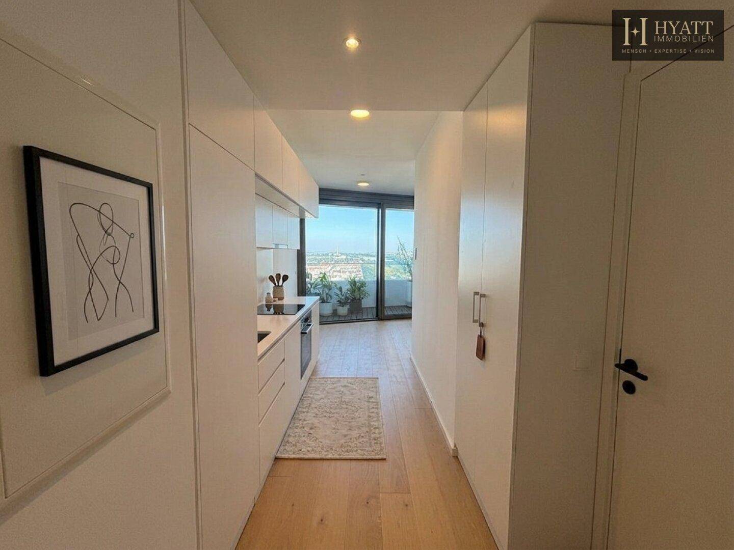 Heller Flur mit integrierten Schränken, der zu einer Küchenzeile und einem Balkon führt.