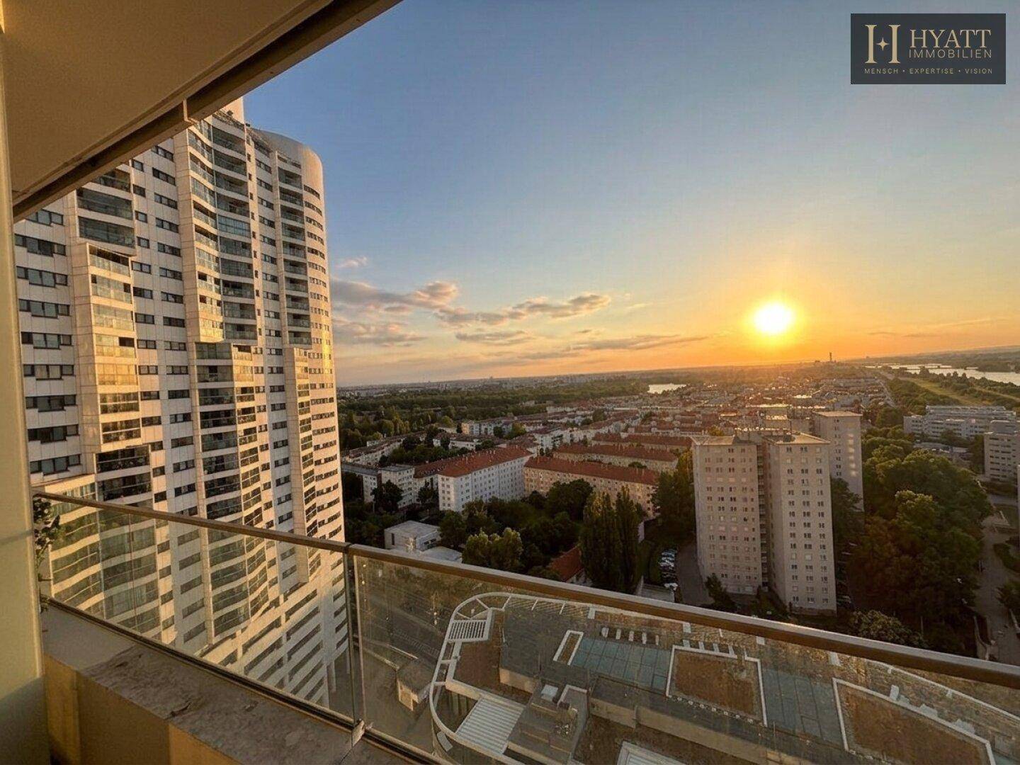 Balkonblick auf ein modernes Hochhaus und die Stadt mit Fluss bei Sonnenuntergang.
