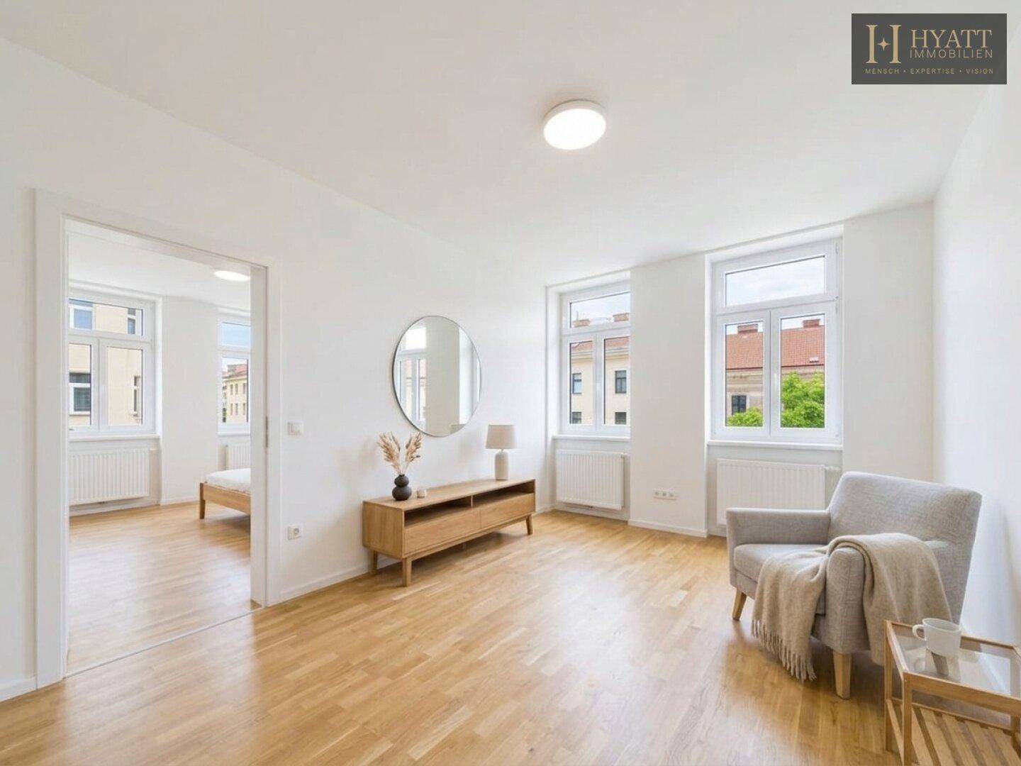 Heller Wohnbereich mit Holzboden, großem Fenster und Zugang zu einem angrenzenden Schlafzimmer.