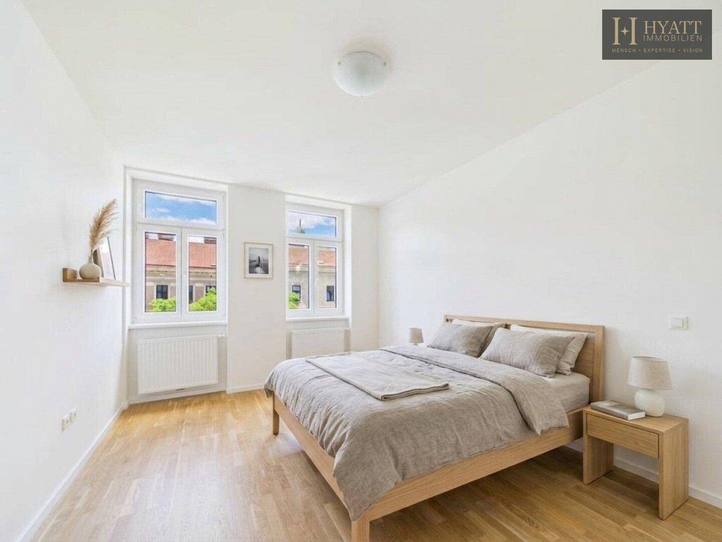Ruhiges Schlafzimmer mit Holzbett, Nachttischen und zwei großen Fenstern mit Stadtblick.
