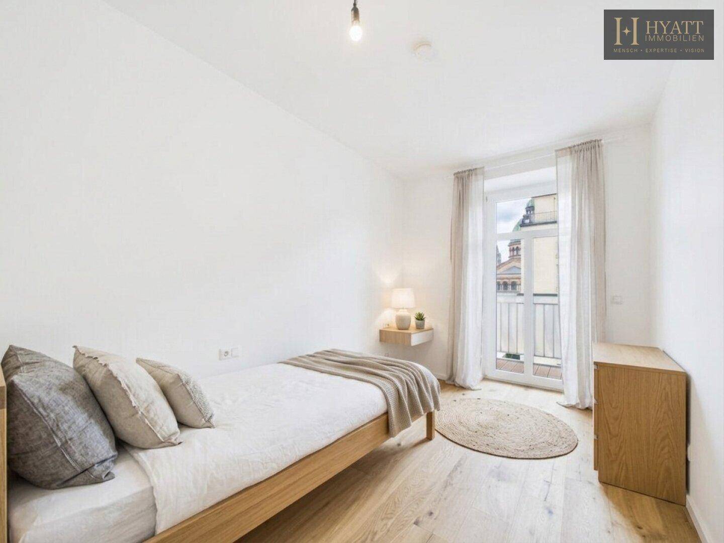 Helles Schlafzimmer mit Holzbett, Parkettboden und Zugang zu einem französischen Balkon.