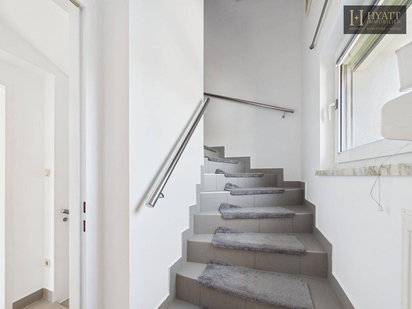 Heller Treppenaufgang mit modernen grauen Stufen und einem schlichten Metallgeländer.