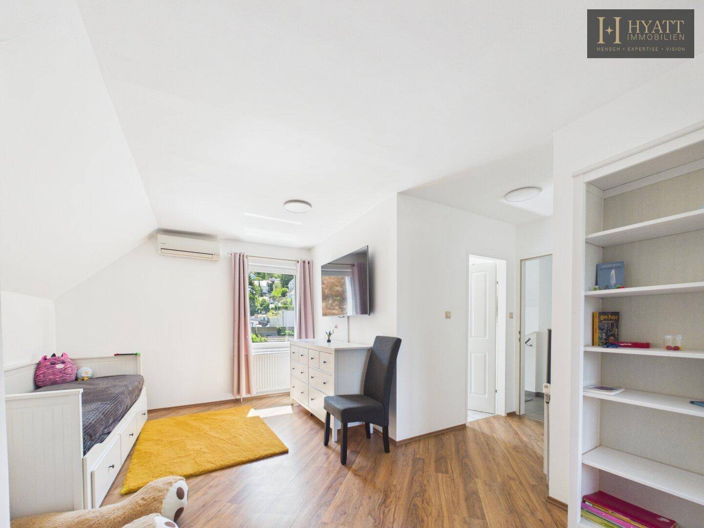 Helles Dachgeschoss-Schlafzimmer mit Einzelbett, Kommode, Fernseher und Fenster mit Ausblick.
