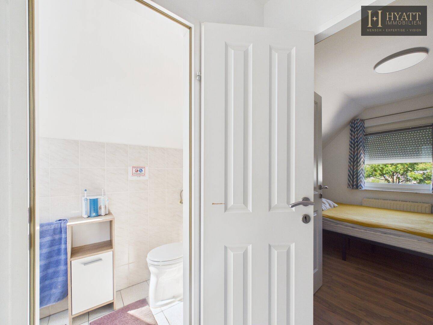 Offene Tür zu einem kleinen WC-Bereich neben einem Schlafzimmer mit Holzboden.