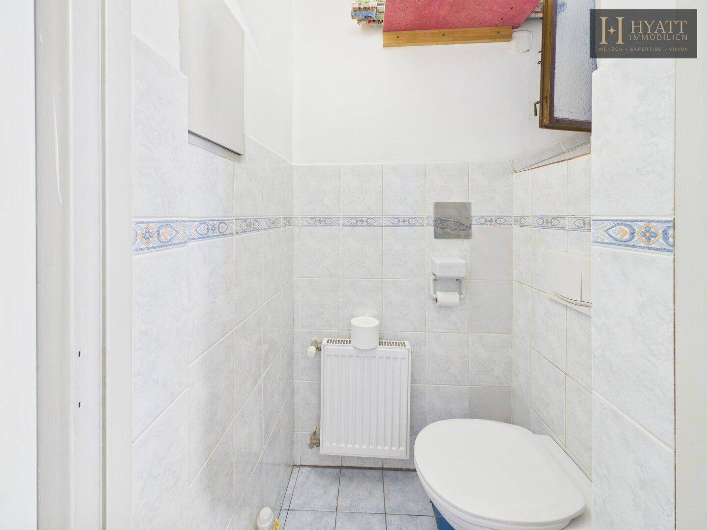 Separates WC mit weißen Fliesen, Toilette und Heizkörper.