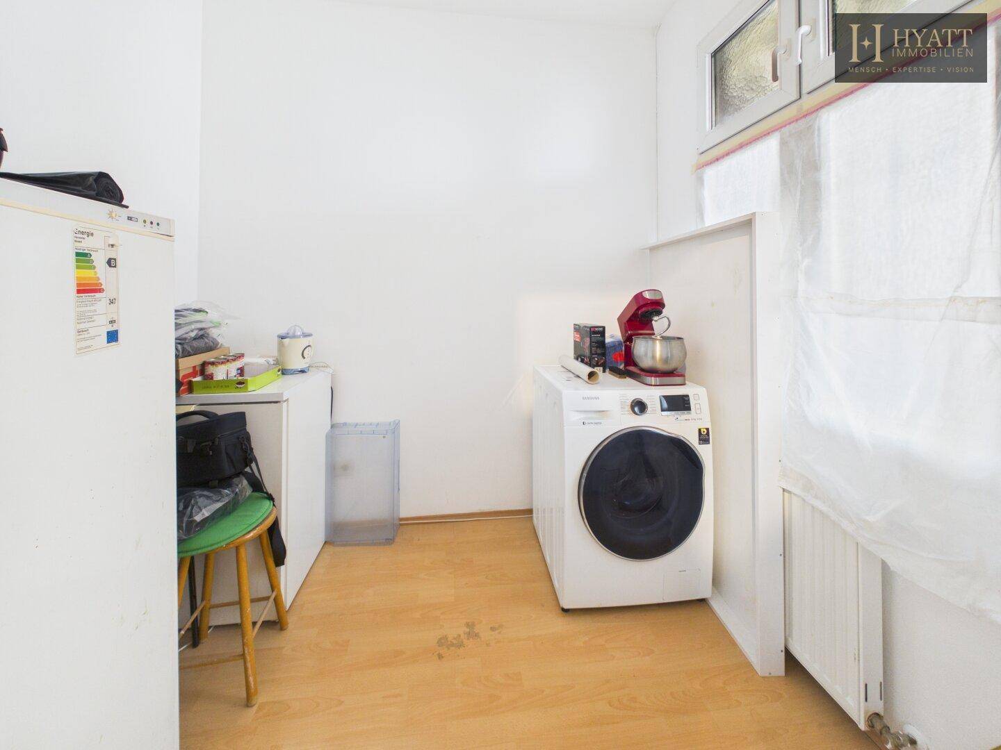 Praktischer Allzweckraum mit Waschmaschine, Kühlschrank und Fenster für Belüftung.