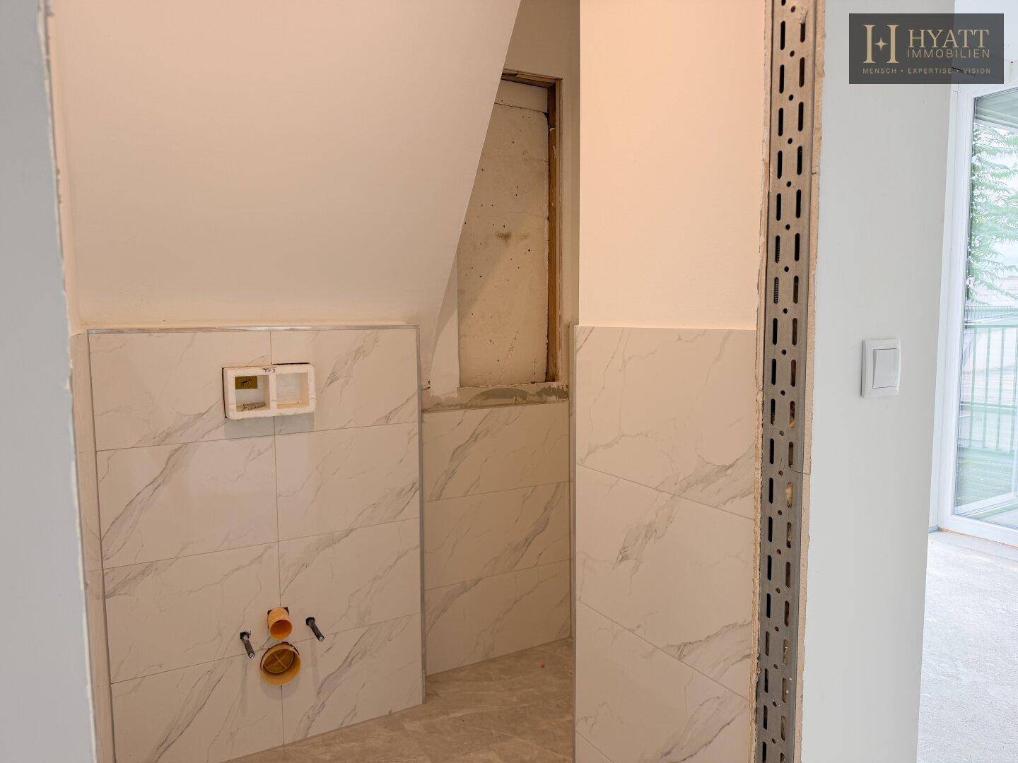 Badezimmer im Rohbau mit Fliesen in Marmoroptik und Vorinstallation für eine Wandtoilette.