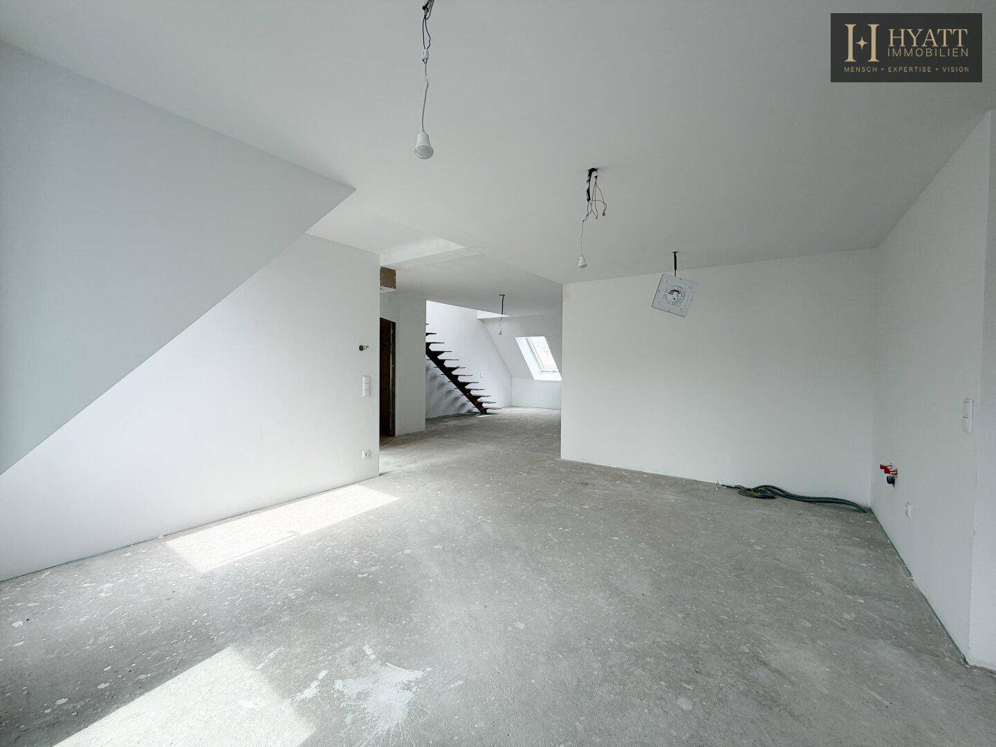 Geräumiger, unmöblierter Wohnbereich im Rohbau mit Treppe und Dachfenstern.
