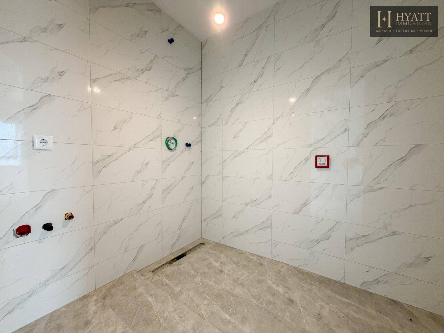 Badezimmer im Rohbau mit modernen Fliesen in Marmoroptik und vorbereiteten Anschlüssen.