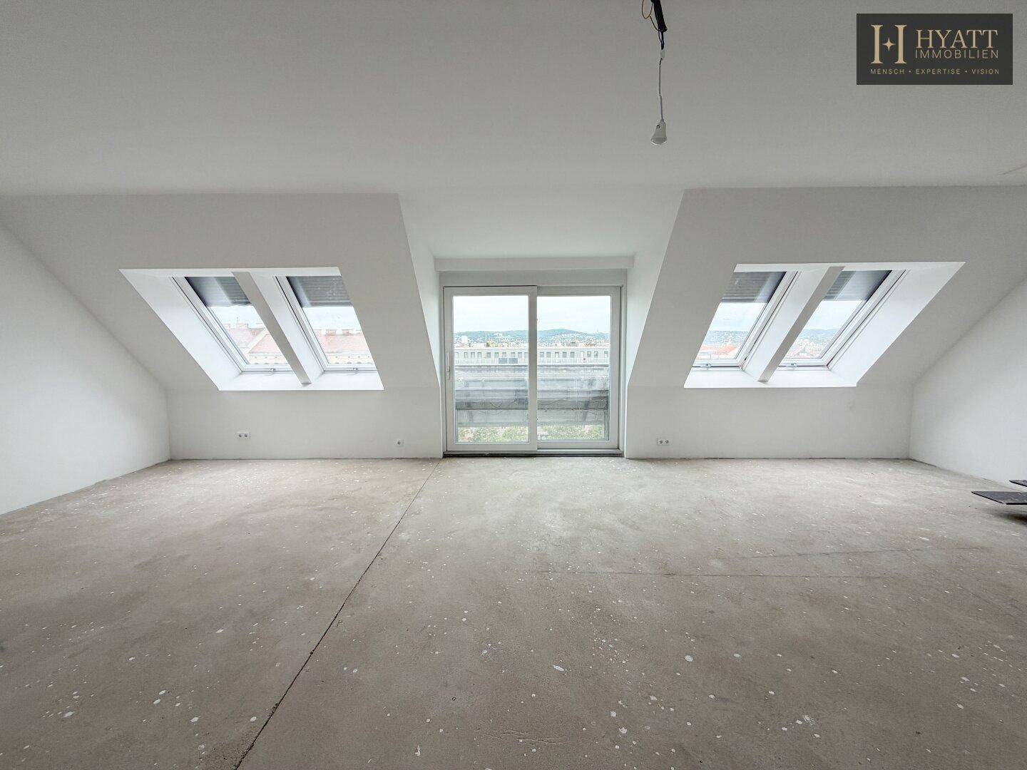 Unmöblierter Raum im Dachgeschoss mit Betonboden, Dachschrägen und Zugang zum Balkon.