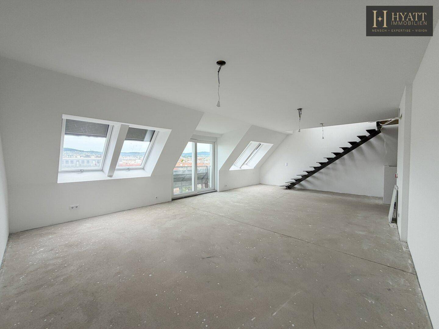 Geräumiger, unmöblierter Dachgeschossraum mit Betonboden, Dachschrägen und offener Treppe.
