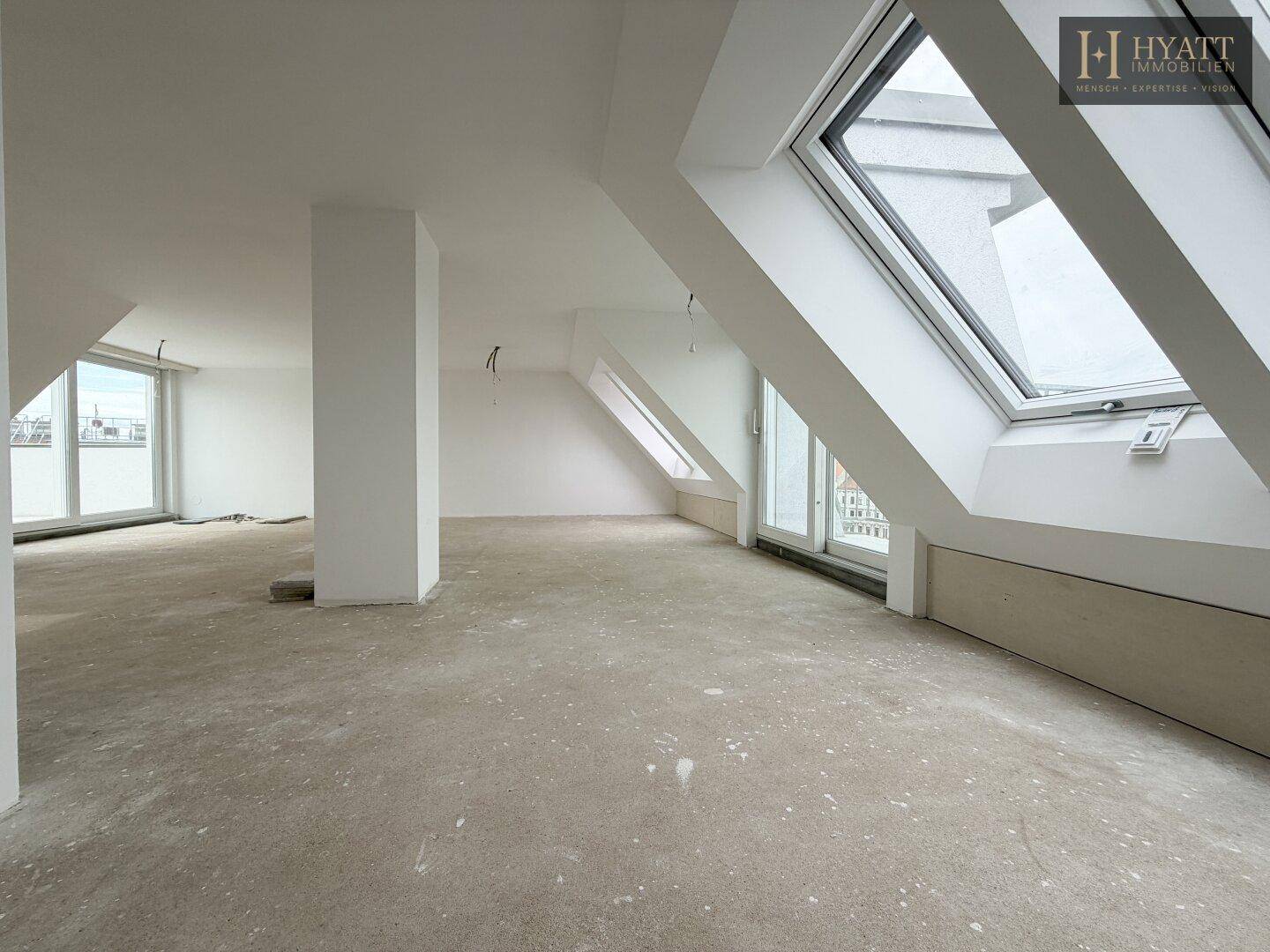 Großer, unmöblierter Raum im Dachgeschoss mit Betonboden und vielen Dachfenstern.