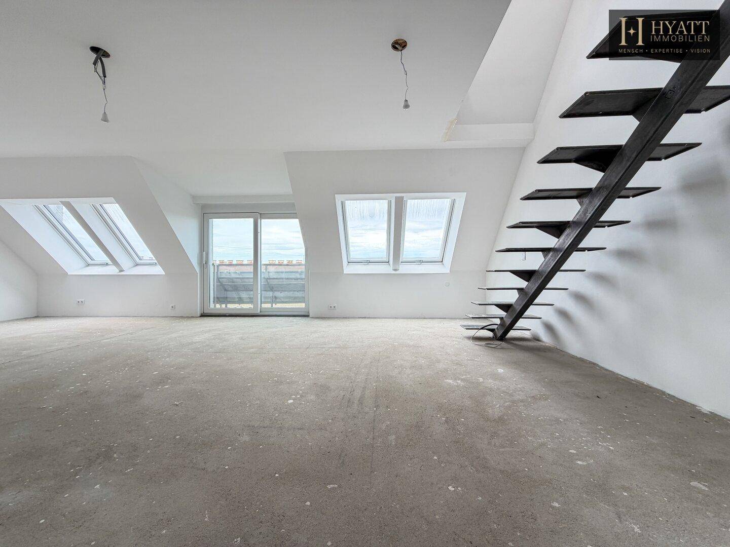 Unmöblierter Dachgeschossraum mit Betonboden, Dachschrägen und offener Treppe.