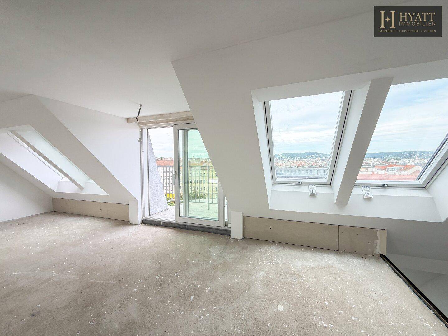 Leerer Dachgeschossraum mit Betonboden, Dachschrägen und Zugang zu einem Balkon.