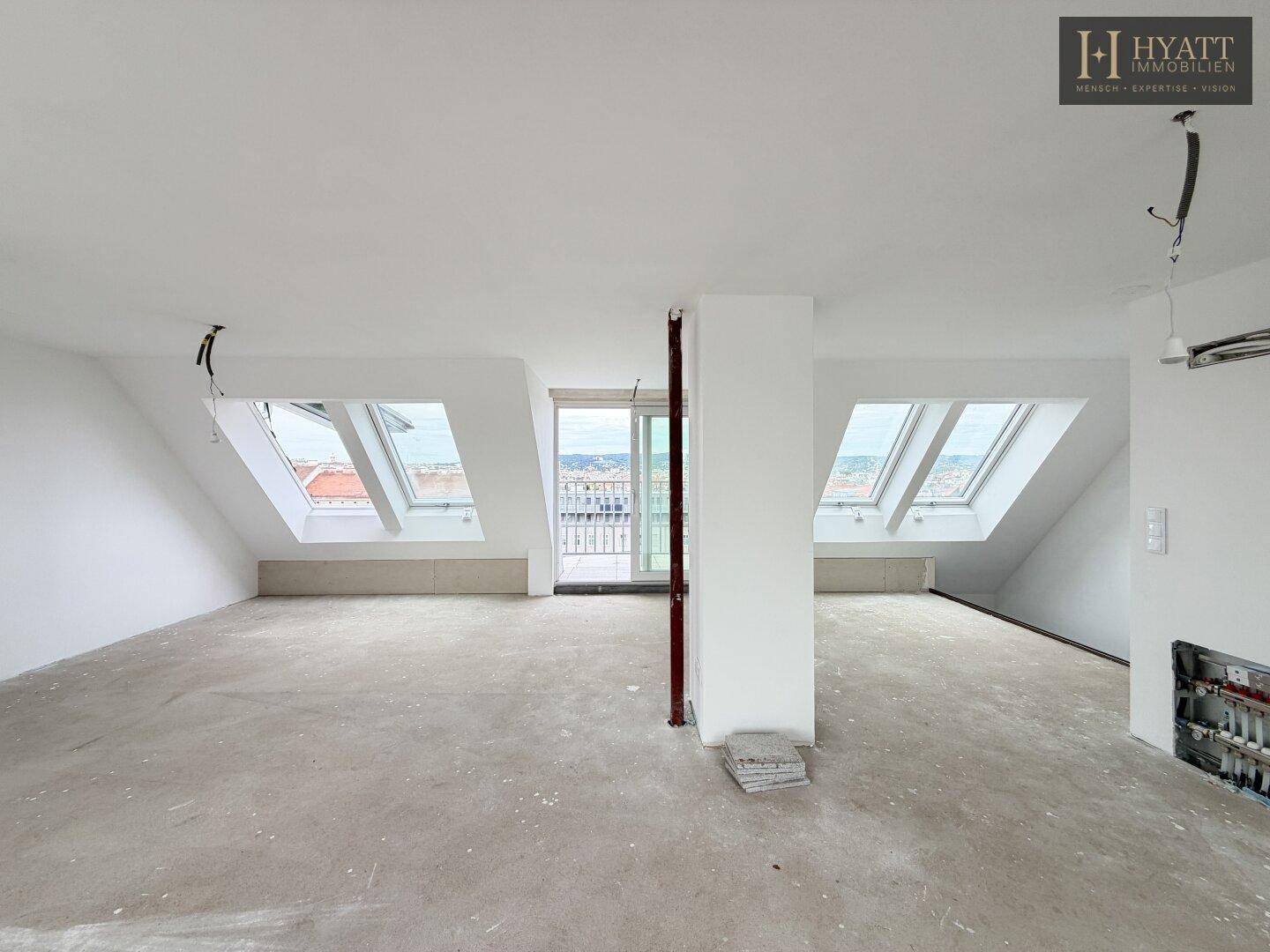 Großer, unmöblierter Dachgeschossraum mit Betonboden, Dachschrägen und vielen Fenstern.