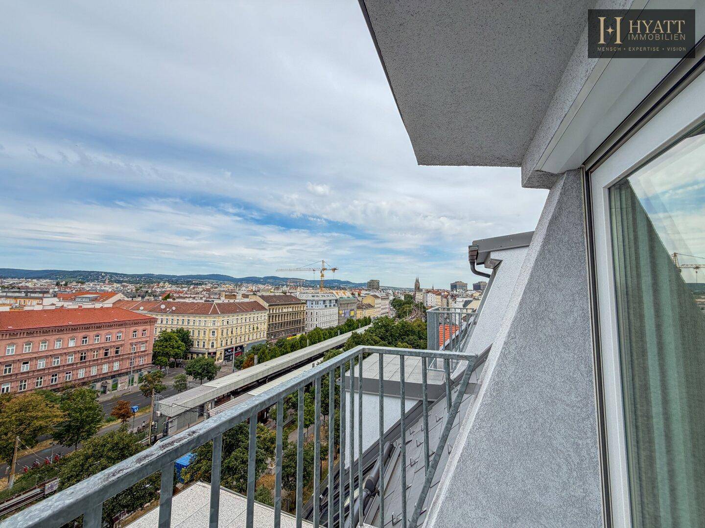 Balkon mit weitem Blick über die Stadt, umgeben von Gebäuden und Grünflächen.