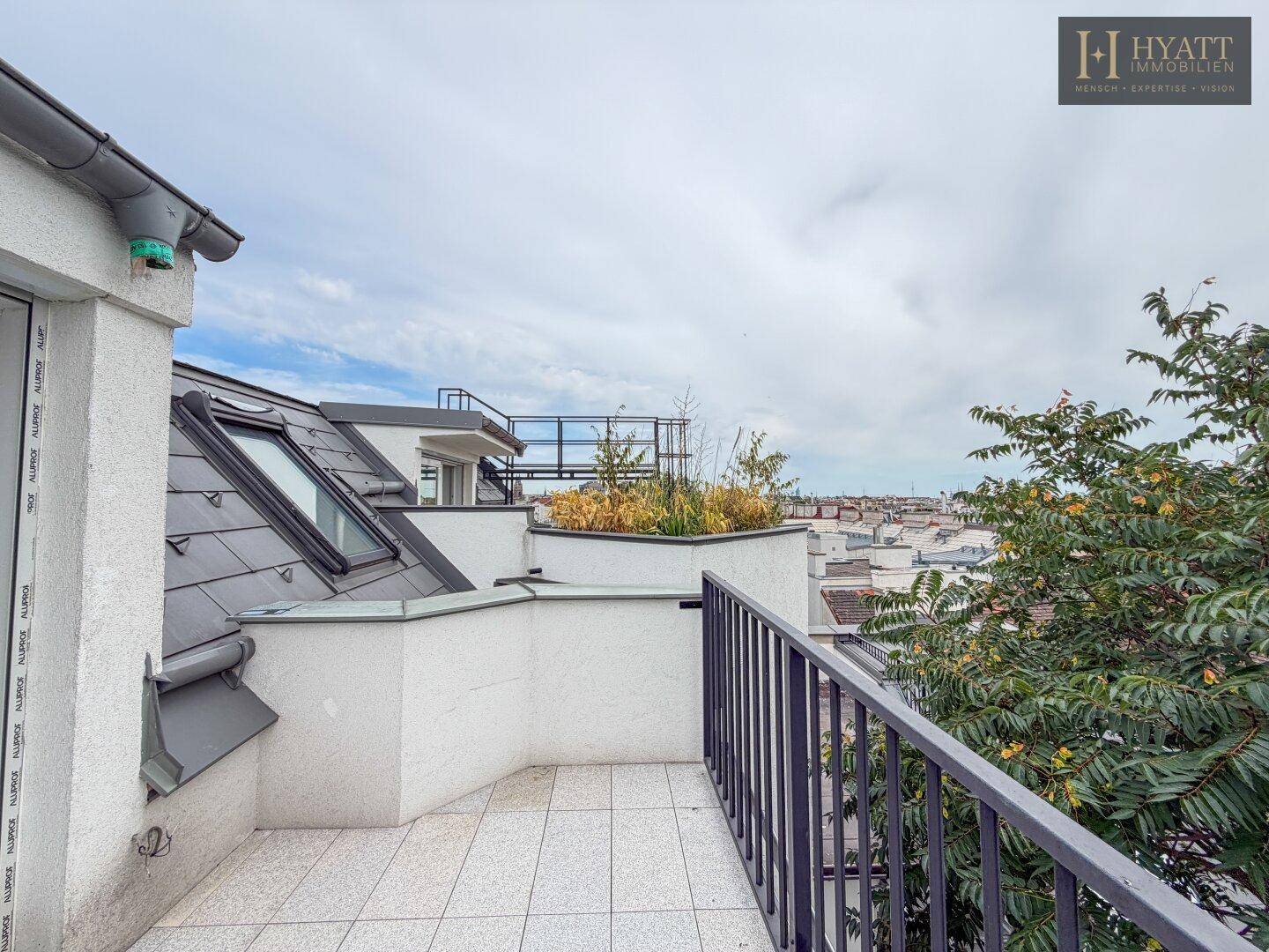Dachterrasse mit Fliesenboden, Schrägdachfenstern und weitem Blick über die Stadtlandschaft.