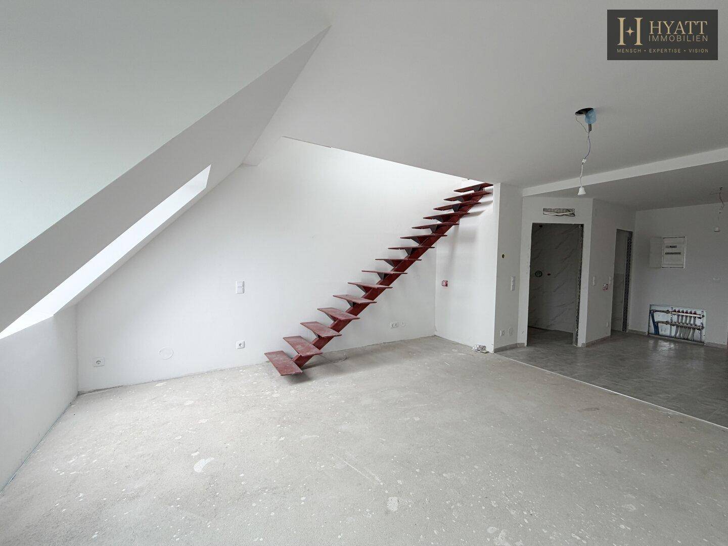 Heller, unmöblierter Raum im Dachgeschoss mit Treppe und Blick auf die Stadt.