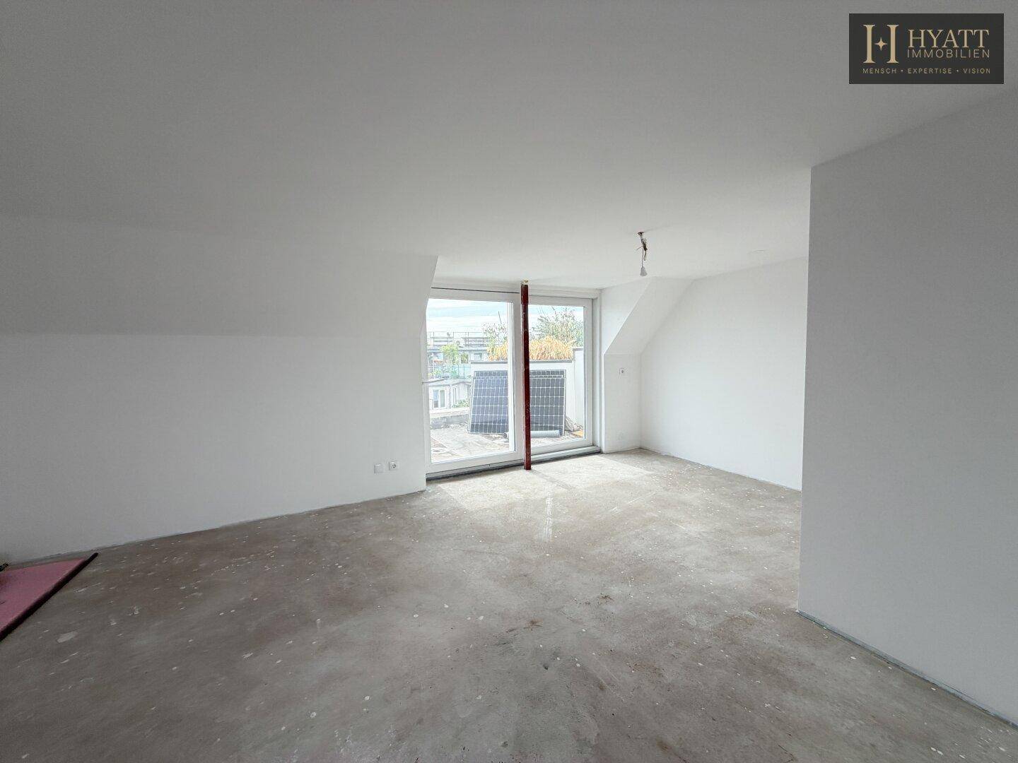 Heller, unmöblierter Raum mit großen Fenstern und Zugang zu einer Terrasse.