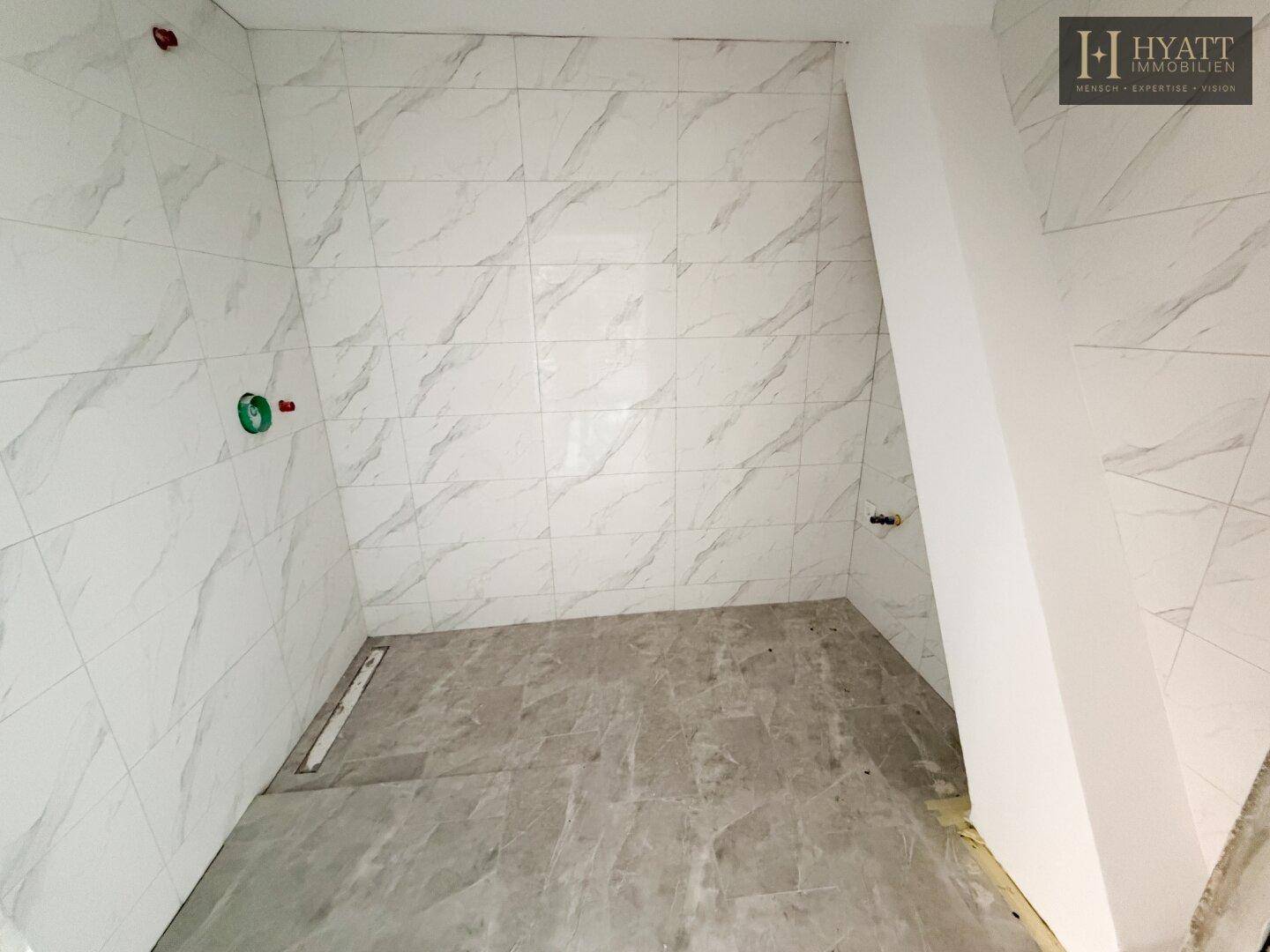 Unfertiges Badezimmer mit Marmorfliesen an Wänden und Boden, vorbereitet für Dusche und Waschtisch.
