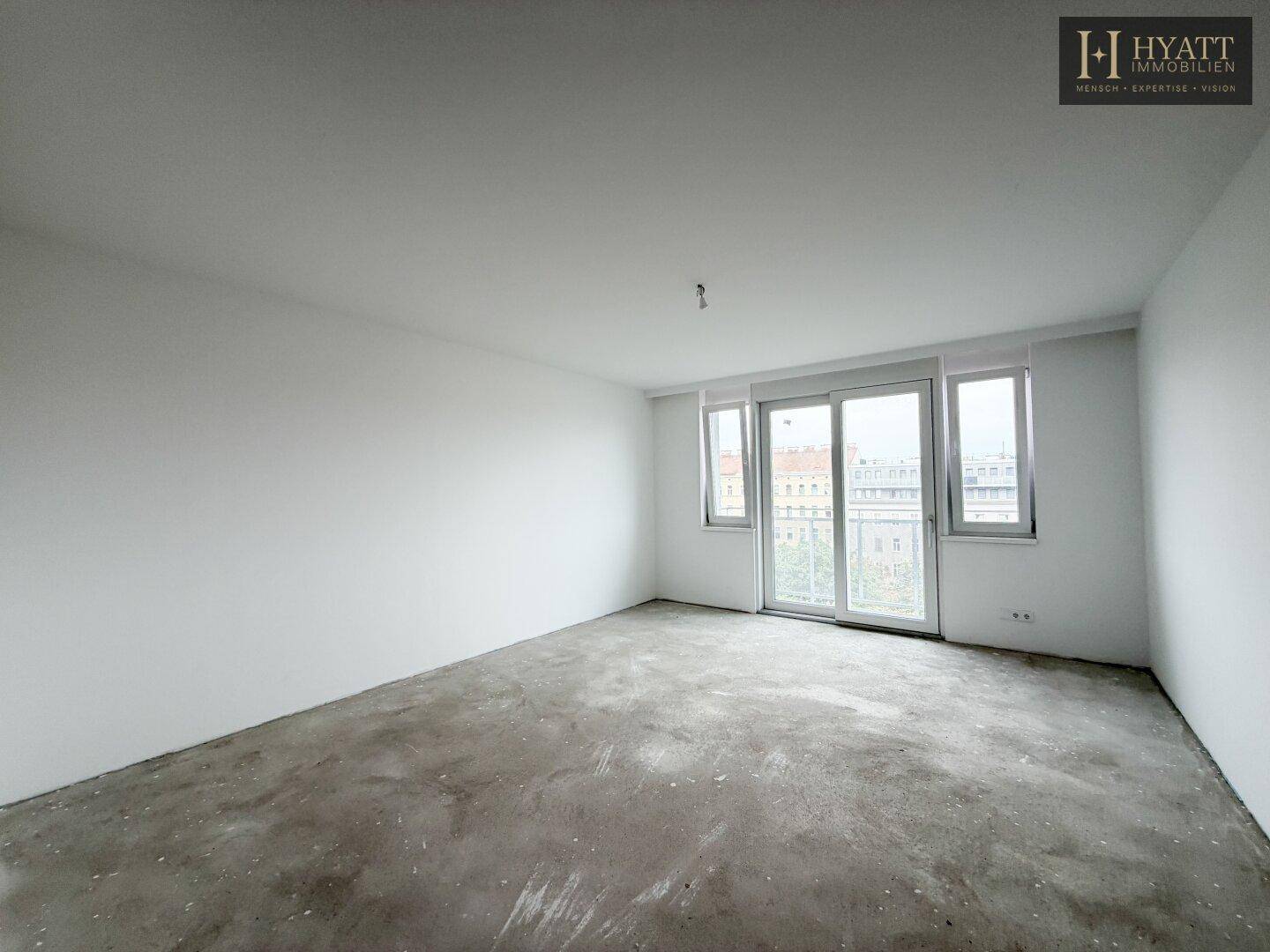 Geräumiger, unmöblierter Wohnbereich mit Rohbetonboden und großen Fenstern, bereit für den Ausbau.