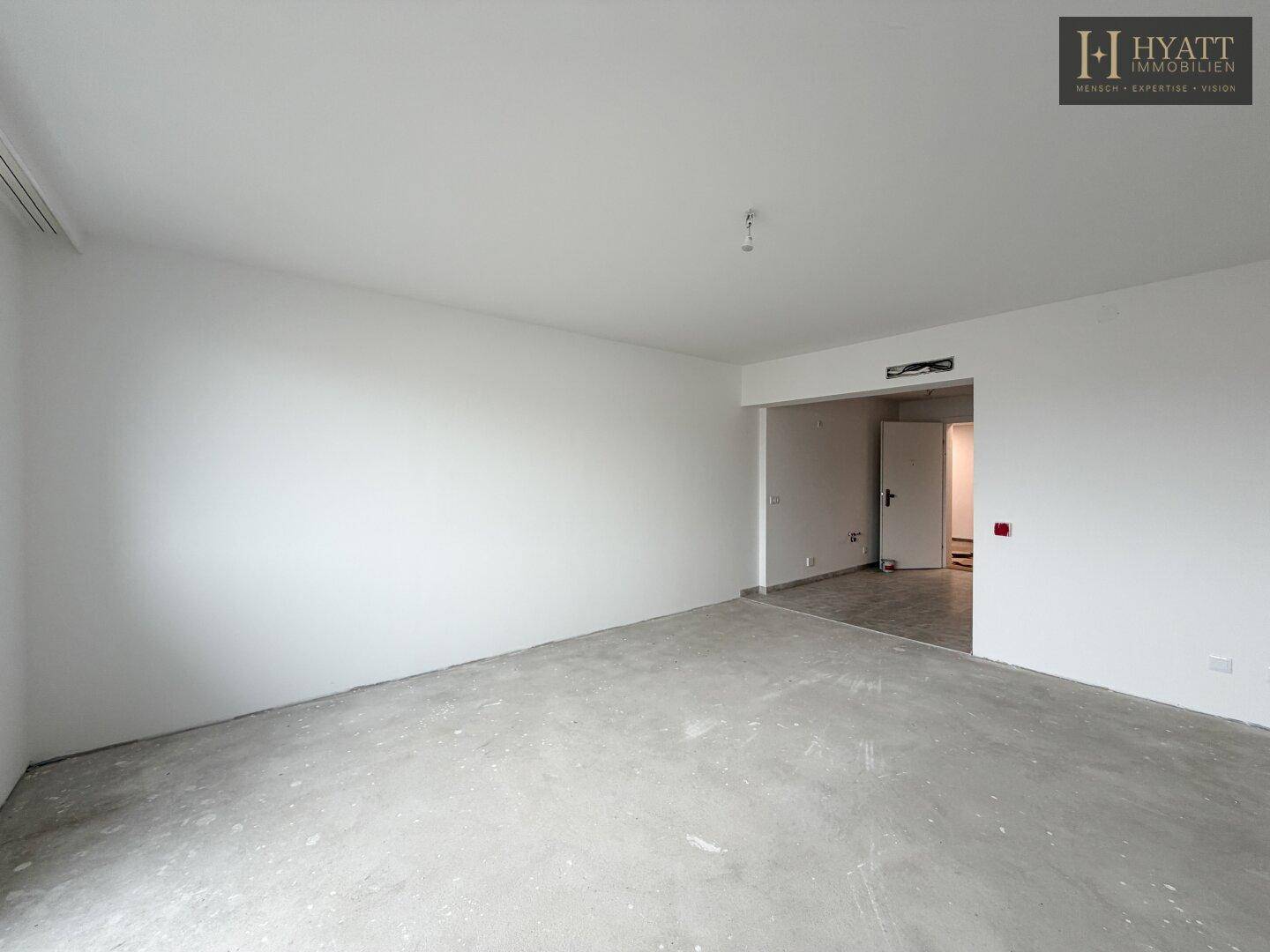Unmöblierter Innenraum mit Rohbetonboden und weiß gestrichenen Wänden, bereit für den Ausbau.