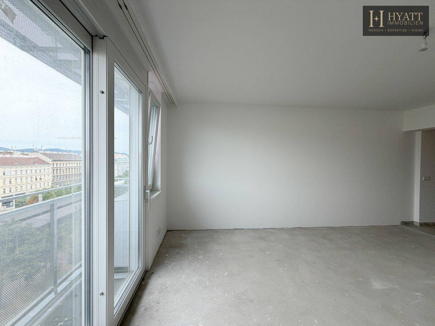 Heller, unmöblierter Raum mit Rohbetonboden und großem Fenster mit Blick auf die Stadt.