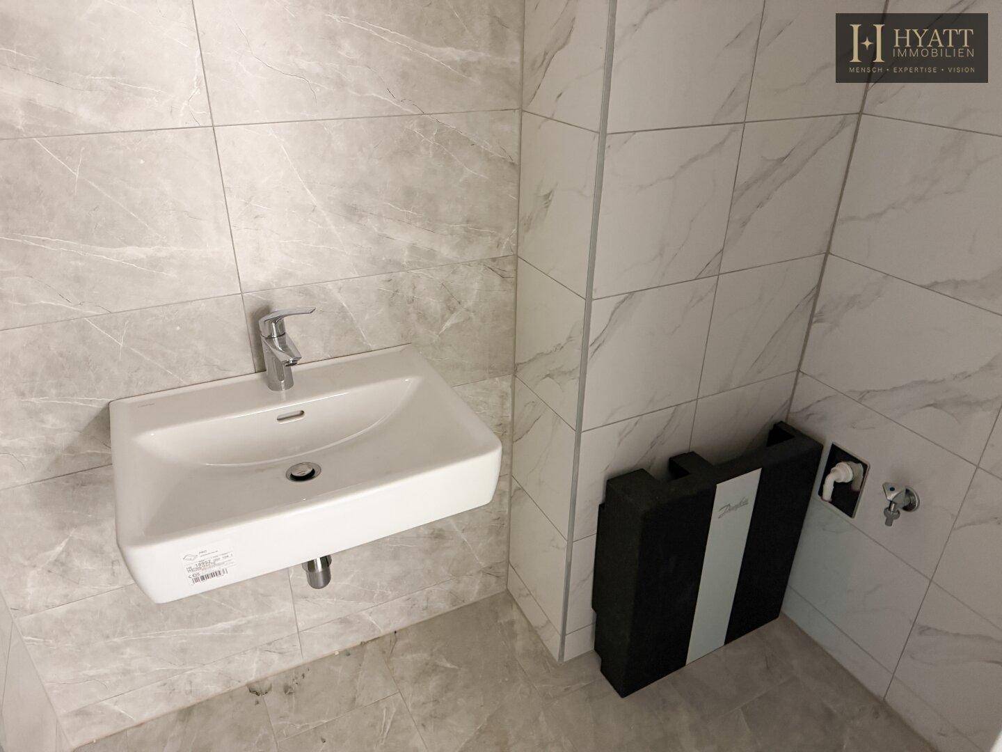 Modern gefliestes Badezimmer mit Waschbecken und Vorbereitung für weitere Sanitärobjekte.