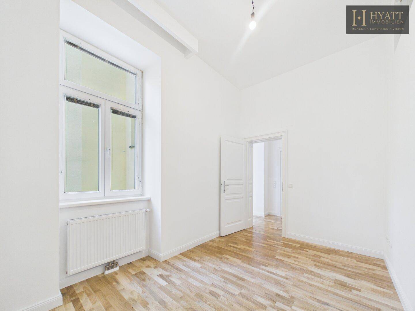 Helles Zimmer mit Parkettboden und großem Fenster, ideal als Schlaf- oder Arbeitszimmer.