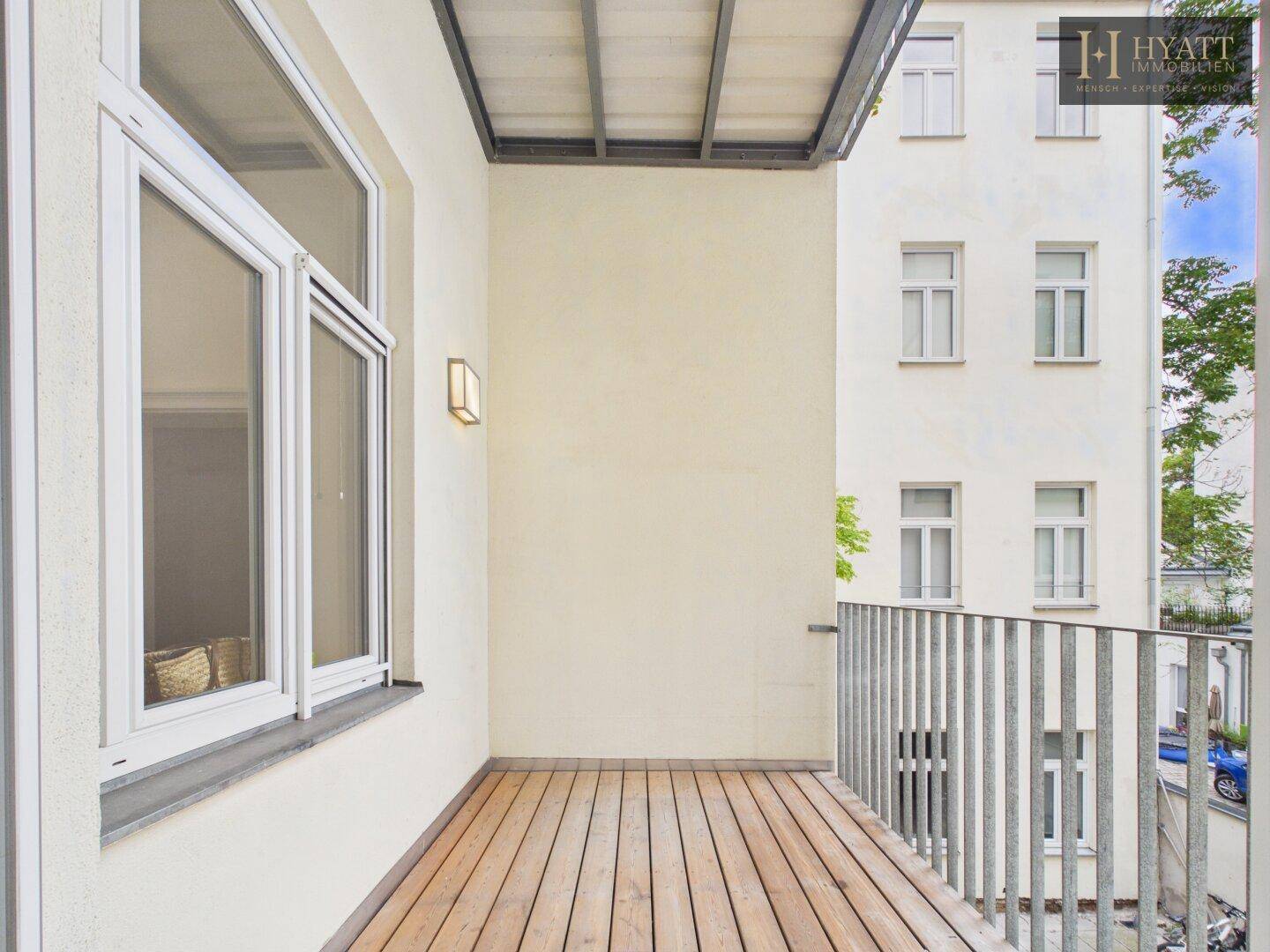 Heller Balkon mit Holzfußboden und Metallgeländer, bietet einen Blick auf die Umgebung.