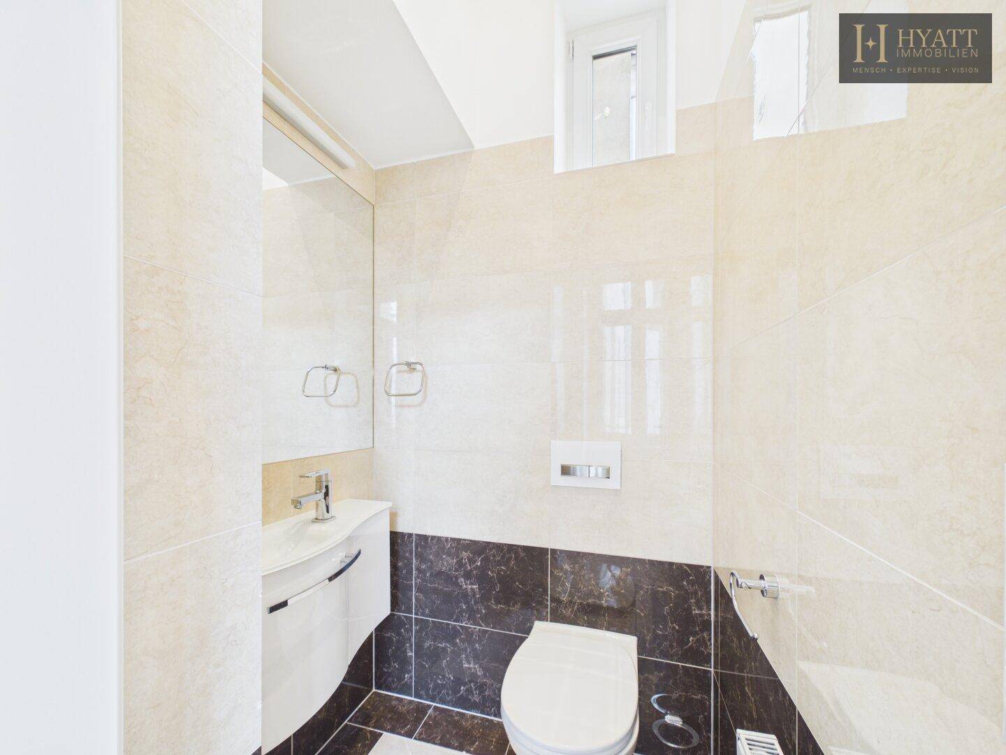 Modernes Gäste-WC mit Wand-WC, kleinem Waschbecken und eleganten Fliesen.