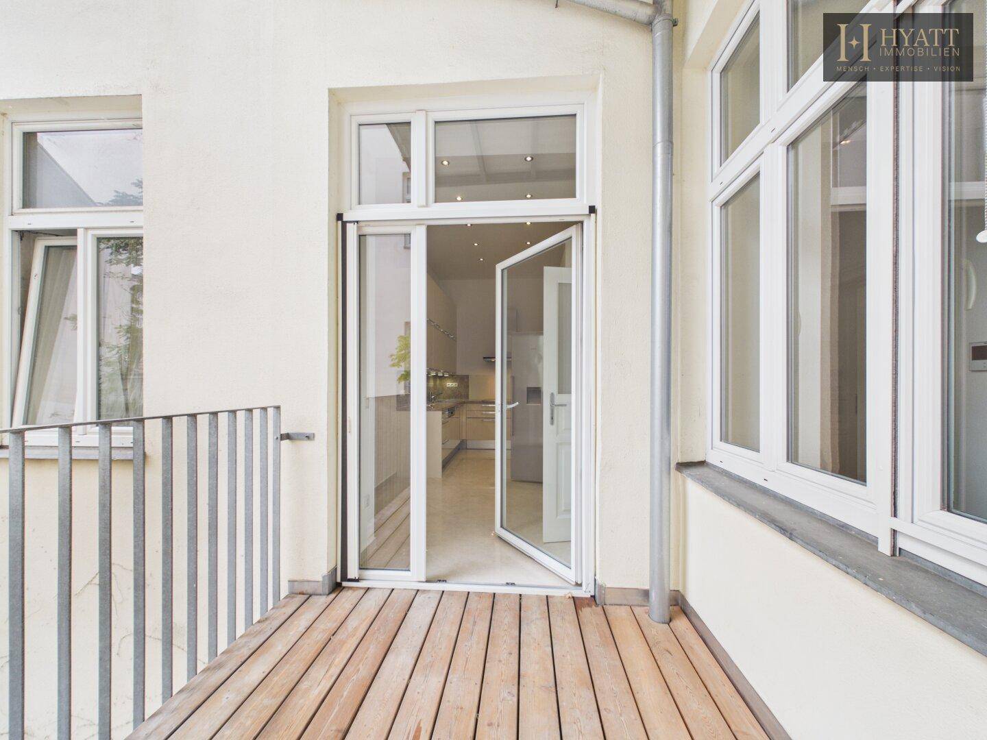 Geräumiger Balkon mit Holzboden und Zugang zur Küche, ideal für Mahlzeiten im Freien.