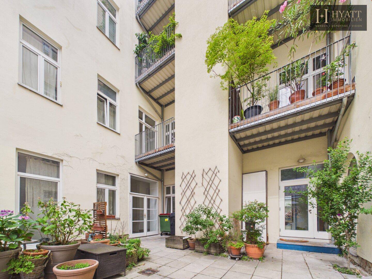 Begrünter Innenhof mit Pflanzen und Balkonen, bietet eine ruhige Rückzugsmöglichkeit.
