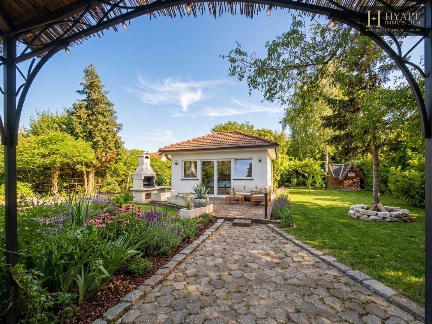 Malerischer Garten mit Blumenbeeten, Grillplatz und Gartenhaus im Hintergrund.