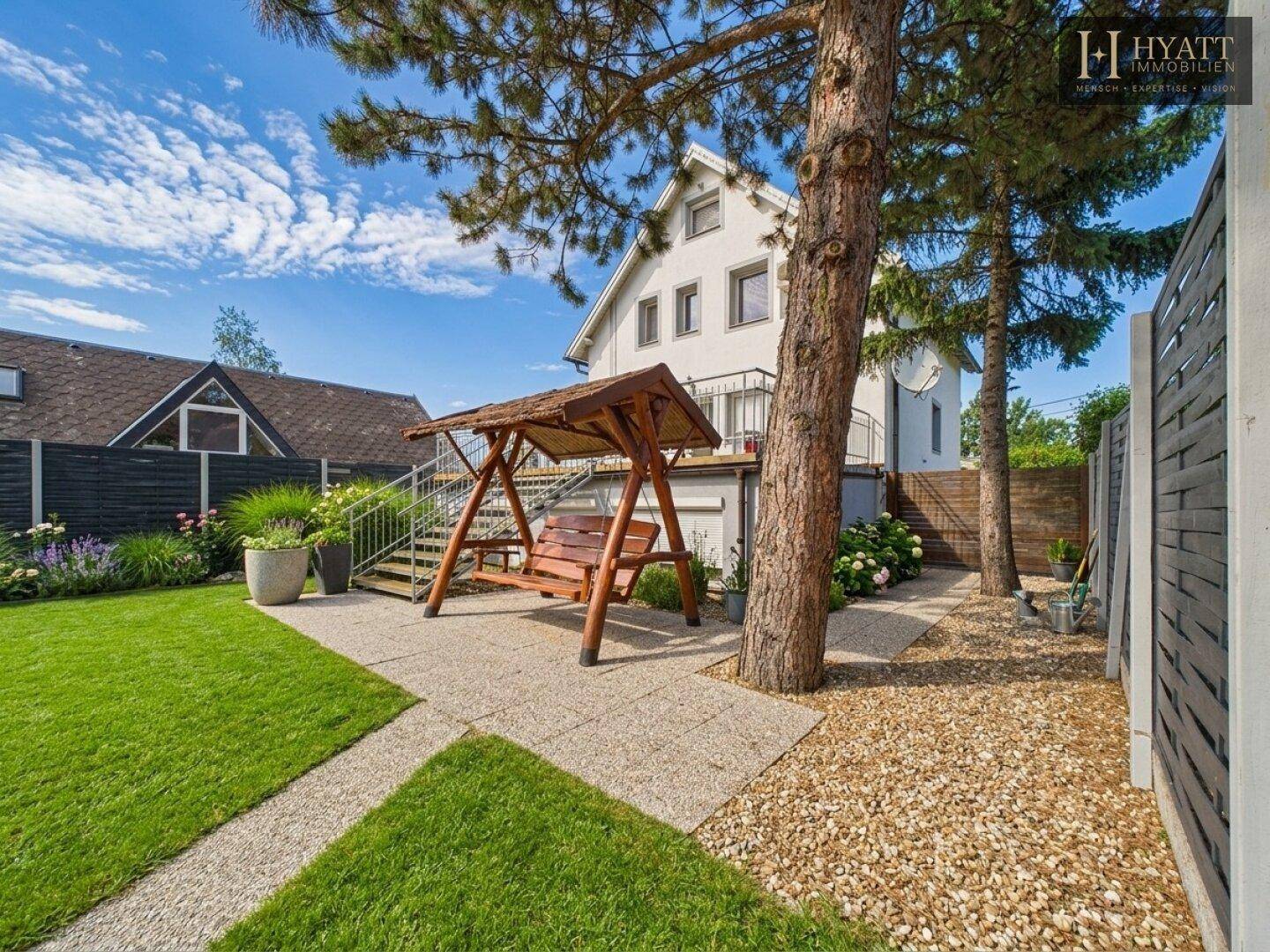 Gepflegter Garten mit Schaukel, Kieswegen und Blick auf das Haus.
