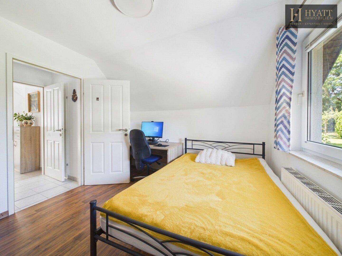 Helles Schlafzimmer mit Einzelbett, Schreibtisch und Blick ins Grüne.