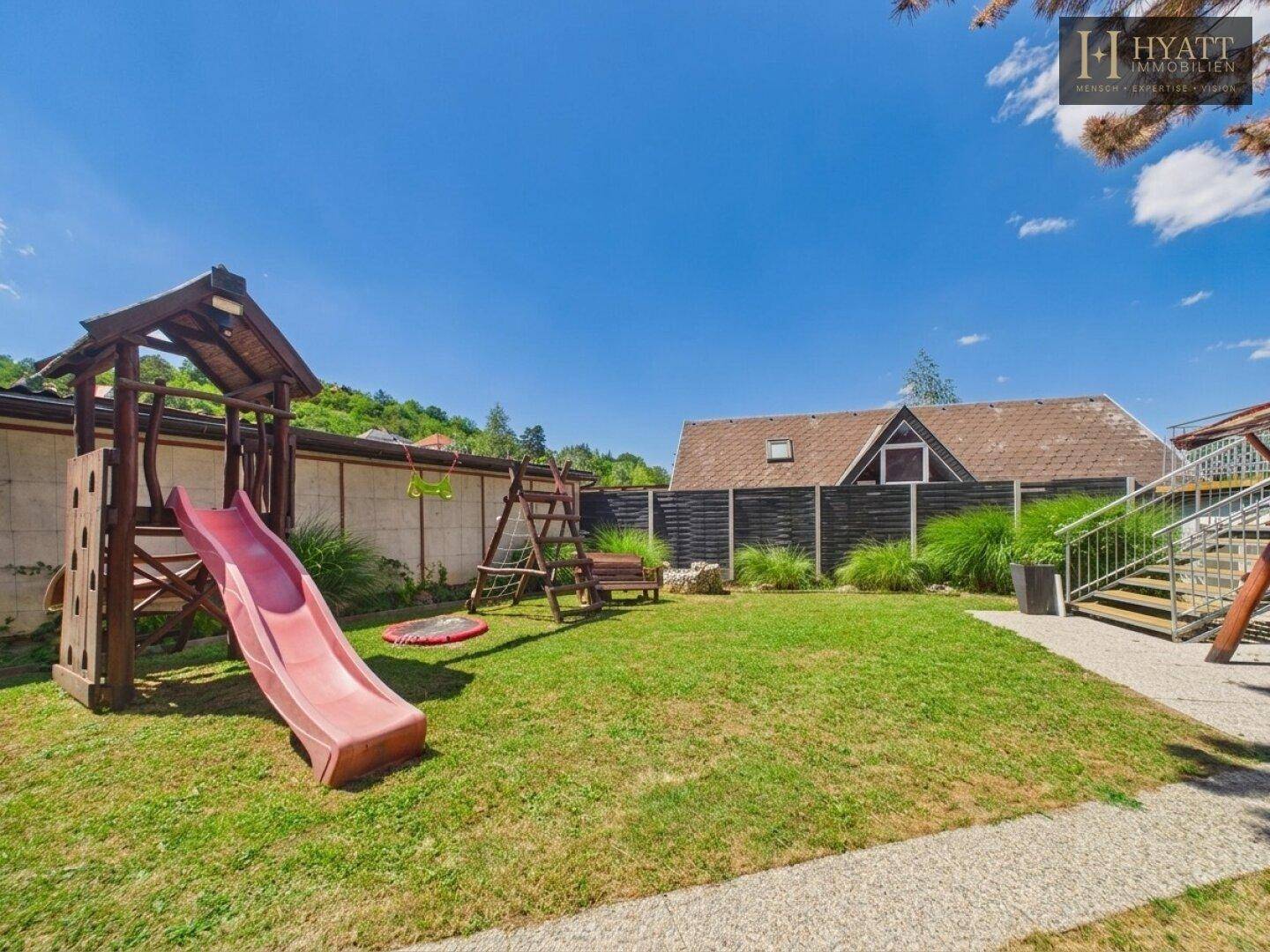 Großer Garten mit Kinderspielplatz, Rutsche und Schaukeln, umgeben von Rasenflächen.