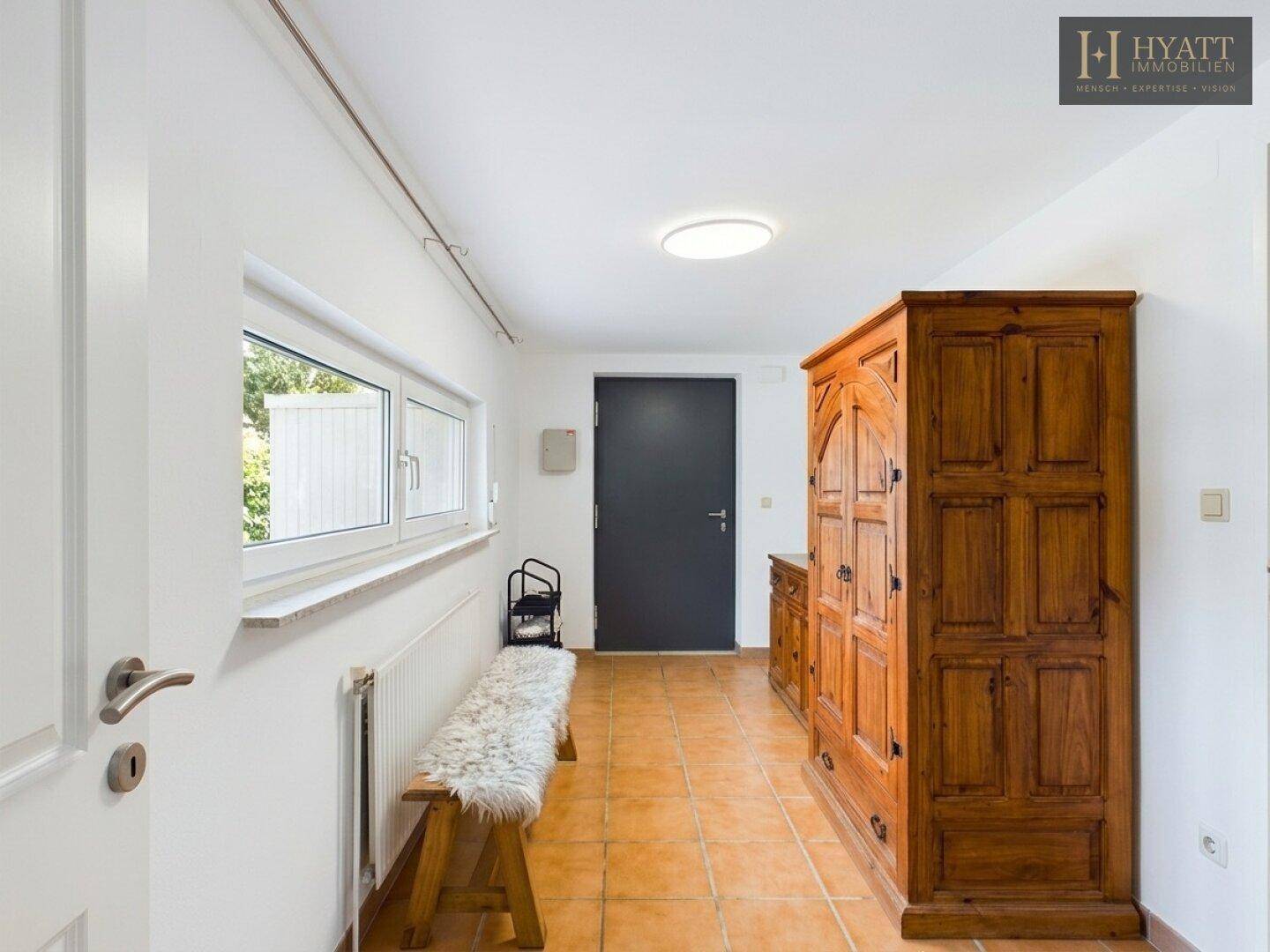 Heller Eingangsbereich mit Terrakotta-Fliesen, Holzschrank und Fenster.