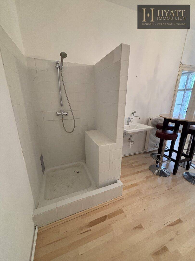 Unkonventioneller Raum mit integrierter Duschkabine, Waschbecken und Bartisch auf hellem Holzfußboden.