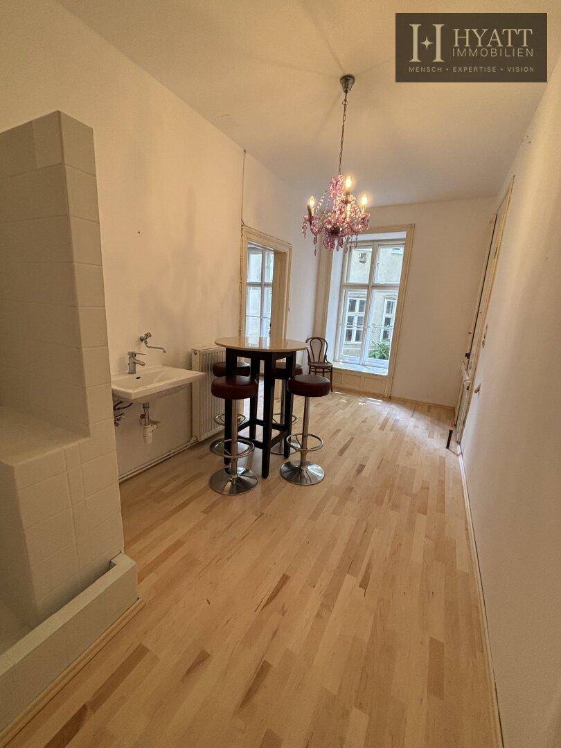 Heller Raum mit Holzboden, Kronleuchter, Bartisch und integriertem Duschbereich im Hintergrund.