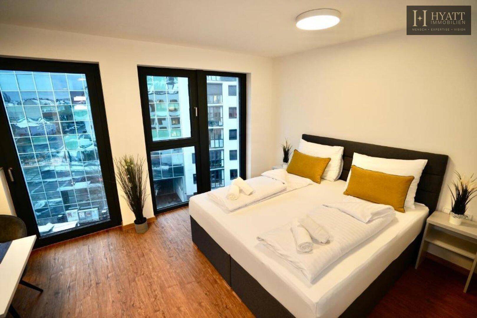 Helles Schlafzimmer mit Doppelbett und großen Fenstern mit Stadtblick.