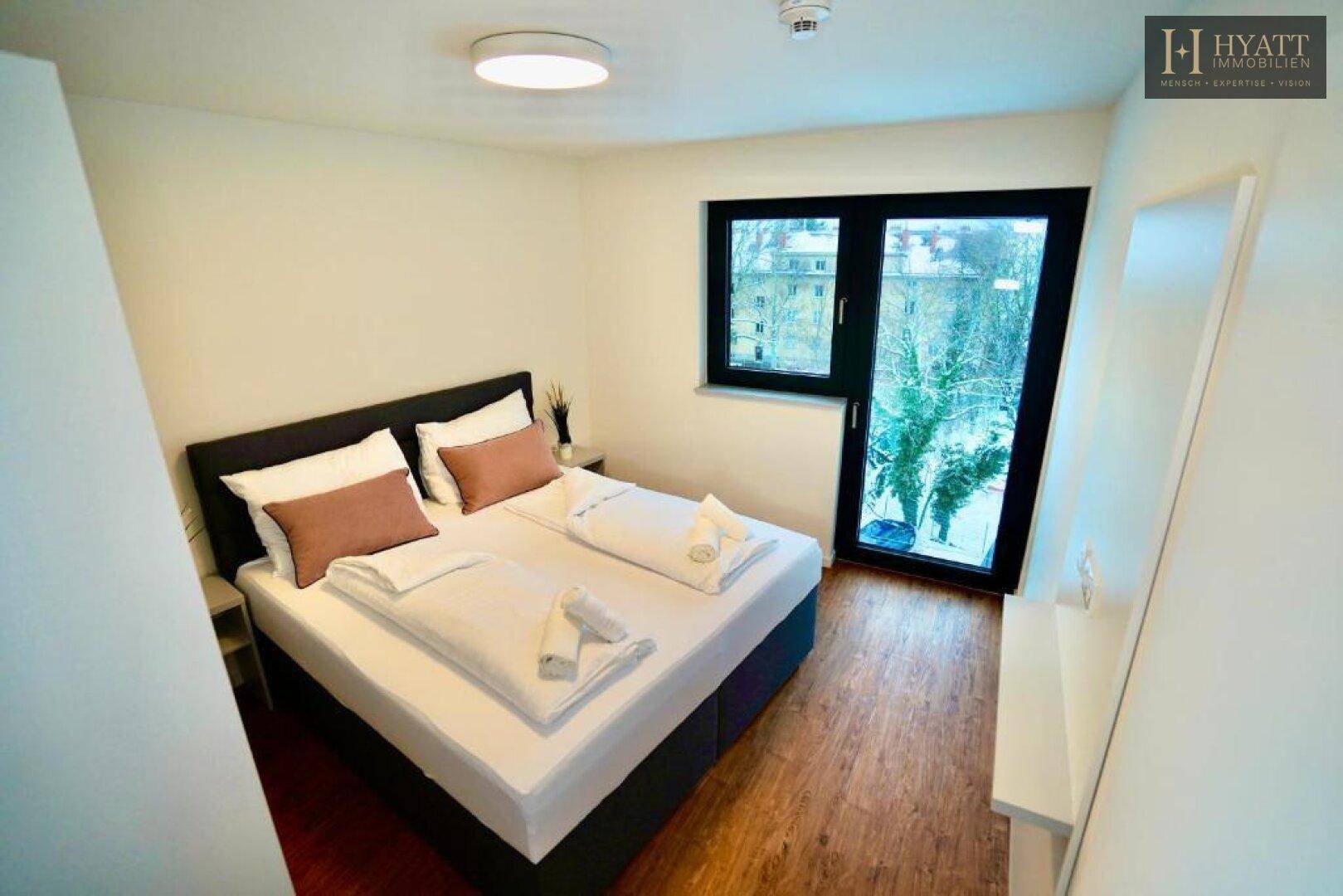 Gemütliches Schlafzimmer mit Doppelbett, Holzboden und großem Fenster mit Blick ins Grüne.
