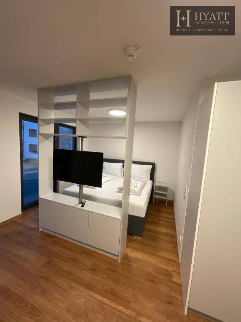 Schlafbereich mit Doppelbett und einem Raumteiler, der einen Fernseher integriert.