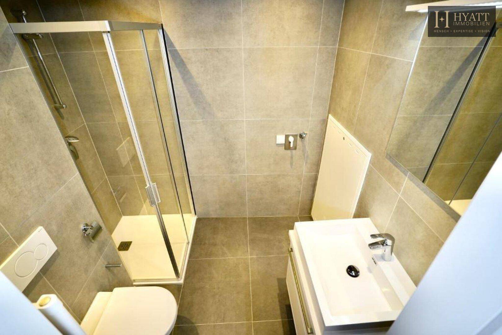 Modernes Badezimmer mit grauen Fliesen, Duschkabine, WC und Einzelwaschbecken.